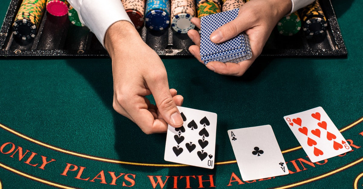 A closeup of poker chips and a blackjack dealer's hands dealing cards on an authentic green blackjack table.