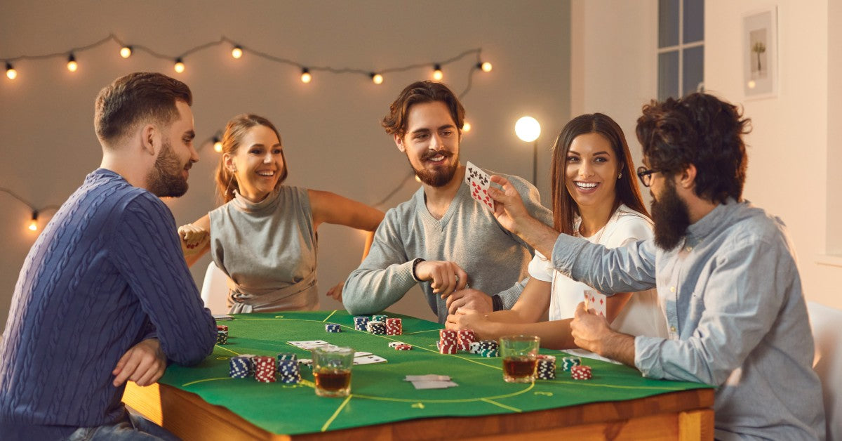 A group of young people playing poker on a home poker table outside with a poker felt and cards, chips, and drinks.