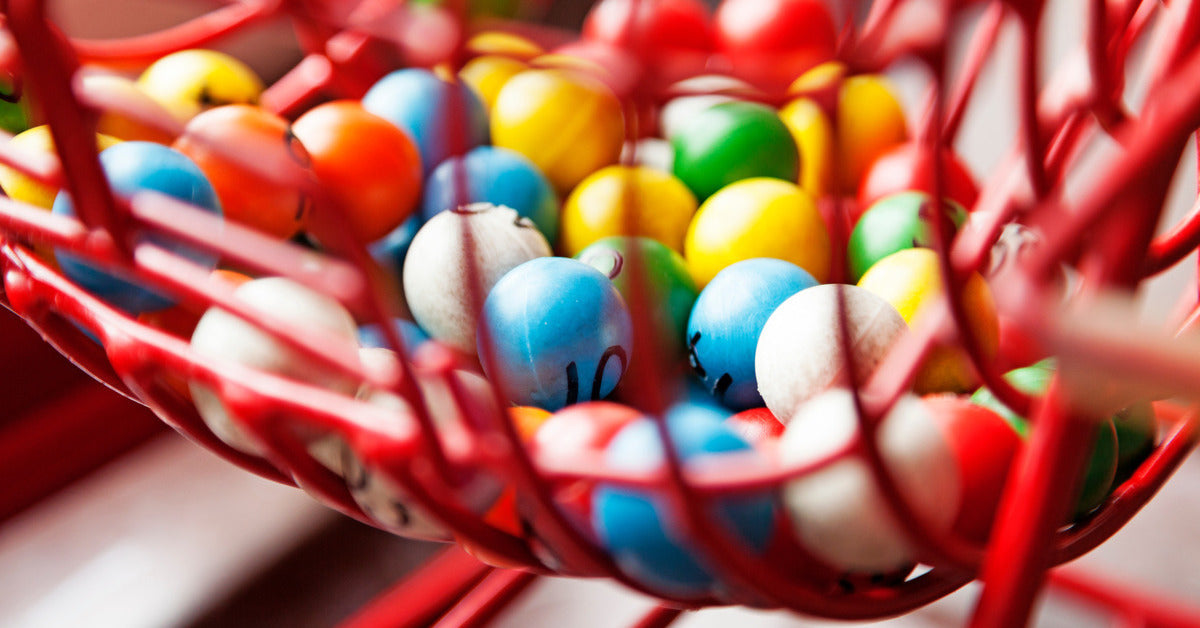 A close-up of a rolling bingo cage filled with bingo balls in various colors. Each ball has a different number on it.