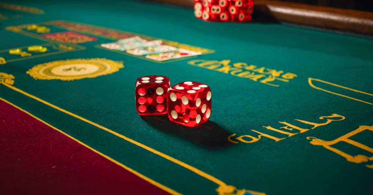 Two red casino dice rest on a green, red, and gold casino craps table with a stack of chips in the background.