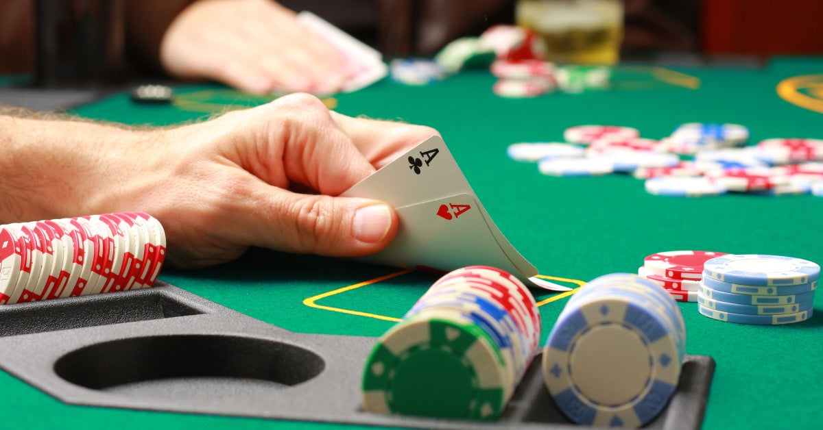 A hand at a green poker table showing his hand of two aces with poker chip stacks next to him and chips in the middle.