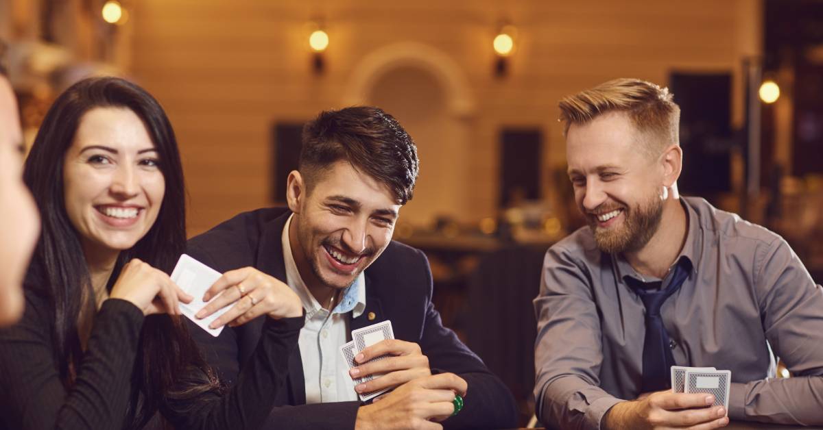 A group of men and women gathered around a blackjack table covered with blue felt and casino chips.