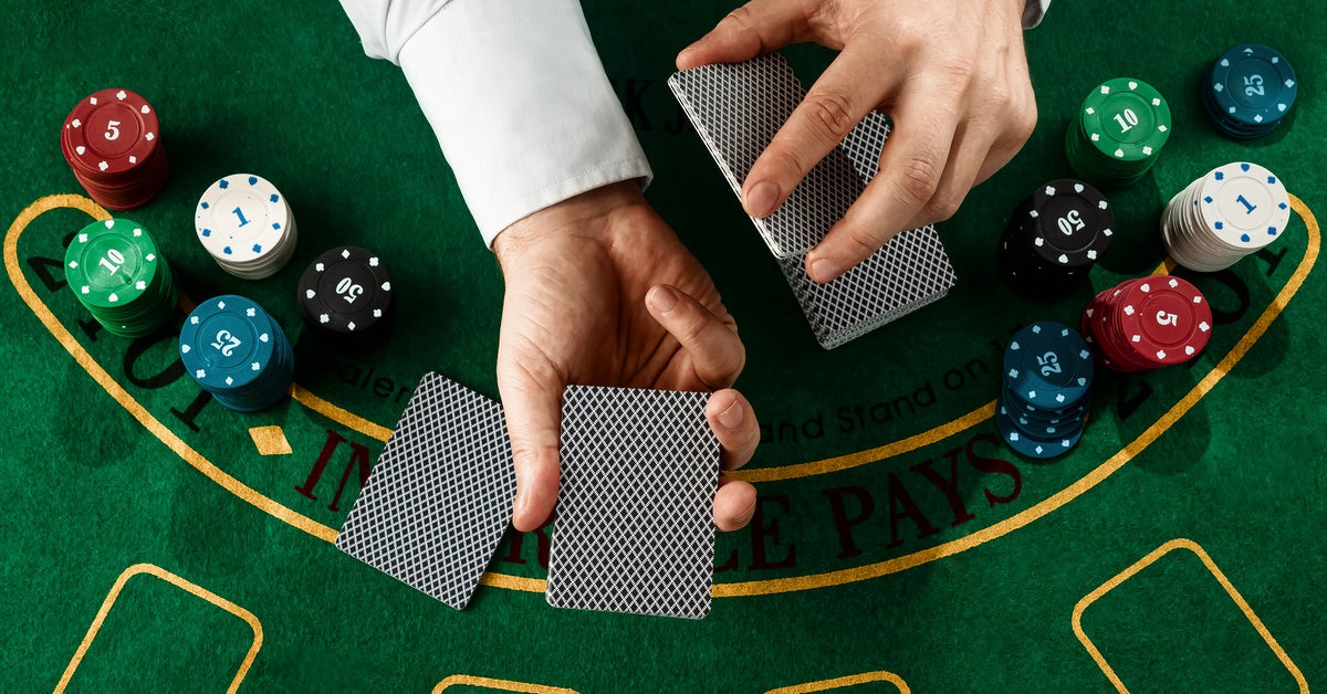 A blackjack dealer holds playing cards facedown as they cut the deck into multiple sections with one in each hand.