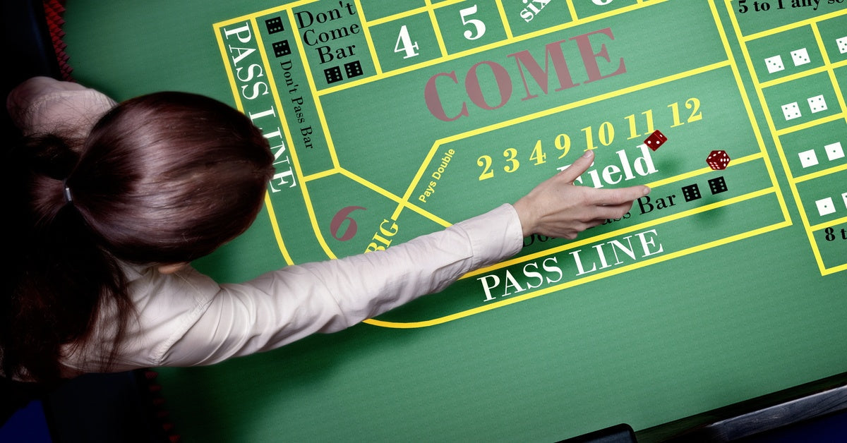 A woman in a white shirt leaning over a craps table throwing red dice across the table's felt surface.